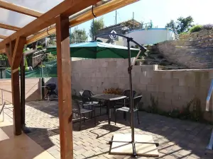 částečně zastřešená terasa se zahradním nábytkem a slunečníkem a nad ní terasovitě řešený pozemek s bazénem