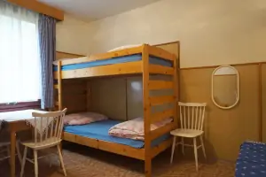 pokoj s rozkládacím gaučem, patrovou postelí, stolem a 4 židlemi