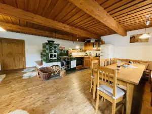 obývací místnost s kuchyňským a jídelním koutem, křesly se stolem a velkými kachlovými kamny s dvojlůžkem 