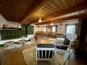 obývací místnost s kuchyňským a jídelním koutem, křesly se stolem a velkými kachlovými kamny s dvojlůžkem 