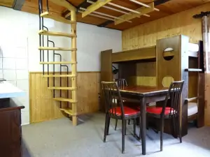 pokoj - stůl, židle, patrová postel a točité schody do podkrovní ložnice