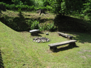 Za chatou za oplocenou zahradou se nachází ohniště s lavičkami