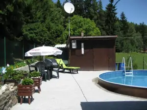 U bazénu se nachází zahradní nábytek se slunečníkem